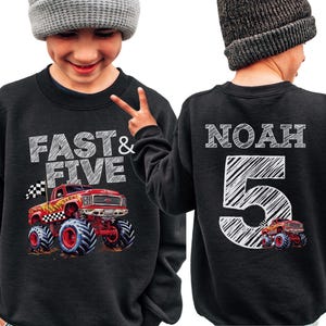 Op de afbeelding: Zwart sweatshirt met een rode en gele monstertruckafbeelding en de tekst "FAST & FIVE" op de voorkant. De achterkant van de sweatshirt heeft de naam "NOAH" en het nummer "5" in het wit gedrukt.