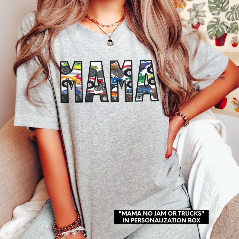 May include: Gray t-shirt with the word "MAMA" spelled out in black letters. The letters are filled with a pattern of colorful trucks and tractors. The text "MAMA NO JAM OR TRUCKS" is printed below the word "MAMA".
