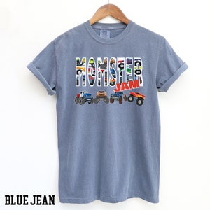 May include: A blue jean t-shirt with a graphic of monster trucks forming the words "Monster Jam".