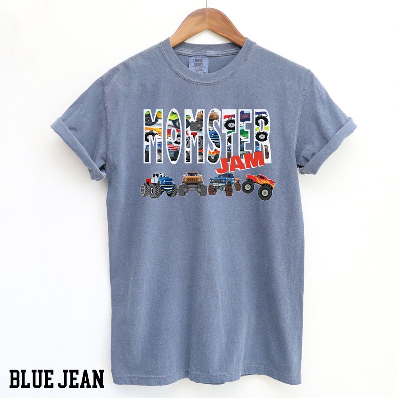 May include: A blue jean t-shirt with a graphic of monster trucks forming the words "Monster Jam".