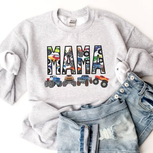 Pictured is a light gray sweatshirt with the word "MAMA" spelled out in  letters that are filled with a colorful pattern of monster trucks. Underneath the custom name are 4 multi-colored monster trucks