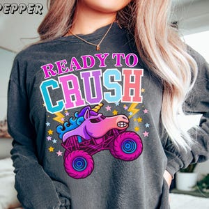 womens monster truck jam sparkle unicorn smash long sleeve comfort colors t-shirt in pepper Grey that says "Ready to Crush" in Multi-Colors Varsity Style Letters Patches with a Unicorn Monster Truck Cartoon Style animal truck  with stars and lightning. Perfect for Monster truck Jam Unicorn Truck Loving Girls, Teens, and Women