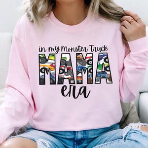Puede incluir: Sudadera rosa de manga larga con el texto "in my monster truck mama era" impreso en la parte delantera. La palabra "mama" est&aacute; formada por im&aacute;genes de monster trucks.