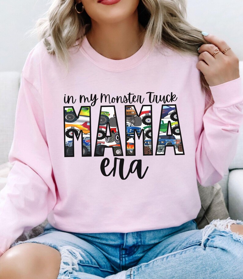 Puede incluir: Sudadera rosa de manga larga con el texto "in my monster truck mama era" impreso en la parte delantera. La palabra "mama" est&aacute; formada por im&aacute;genes de monster trucks.