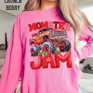 May include: Pink long-sleeved shirt with a graphic of a red monster truck with flames and the text "Momster Jam" in red letters with strawberry accents.