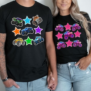 May include: Black t-shirts with colorful monster truck and star graphics. One shirt features various monster trucks, while the other showcases unicorn monster trucks. The designs include green, blue, orange, purple, and yellow trucks.