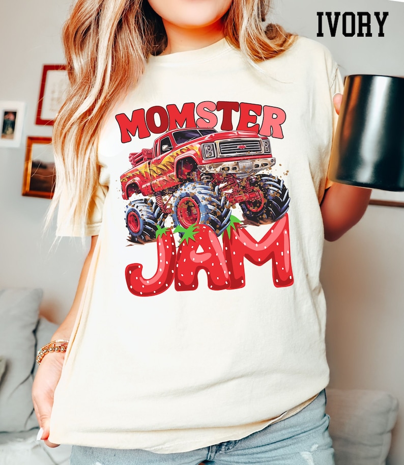 May include: A white t-shirt with a red monster truck graphic and the text "Momster Jam" in red and white letters. The truck is driving through a strawberry field.