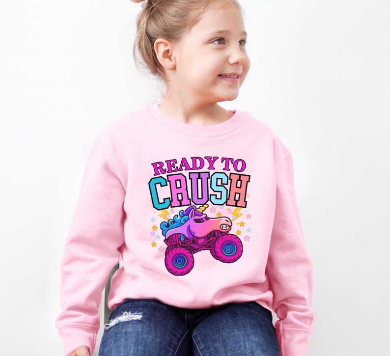 Pu&ograve; includere: Una felpa rosa chiaro con la scritta "READY TO CRUSH" in rosa e turchese. Sotto il testo c'&egrave; un camion mostro dei cartoni animati con una testa di unicorno, nelle tonalit&agrave; del viola, rosa e blu. Il camion ha ruote rosa ed &egrave; decorato con stelle e fulmini.