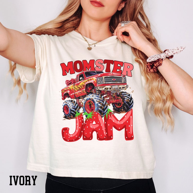 May include: A white t-shirt with a red monster truck graphic and the text "Momster Jam" in red and white letters. The truck is driving through a strawberry field.