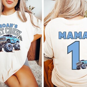 Cream-colored t-shirt featuring a blue monster truck graphic with the text "NOAH'S PIT CREW" on the front. The back of the shirt displays the word "MAMA" above a large number "1" and a smaller monster truck graphic.