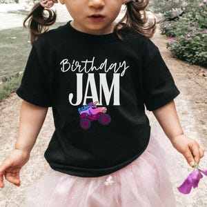 May include: Black t-shirt with the words "Birthday JAM" in white script and block letters. A colorful graphic of a unicorn monster truck is below the text. The shirt is worn by a child.