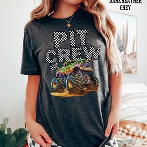 May include: Dark heather grey t-shirt with the words "PIT CREW" in a checkered pattern. A colorful monster truck graphic is featured below the text. The shirt is a comfortable, casual style.