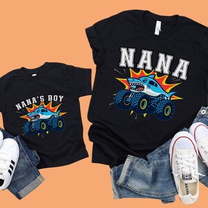May include: Black t-shirts with matching shark monster truck graphics. One shirt says "NANA" and the other says "NANA'S BOY". The shark is light blue with a white belly and a menacing grin. The monster truck has blue tires with yellow accents.