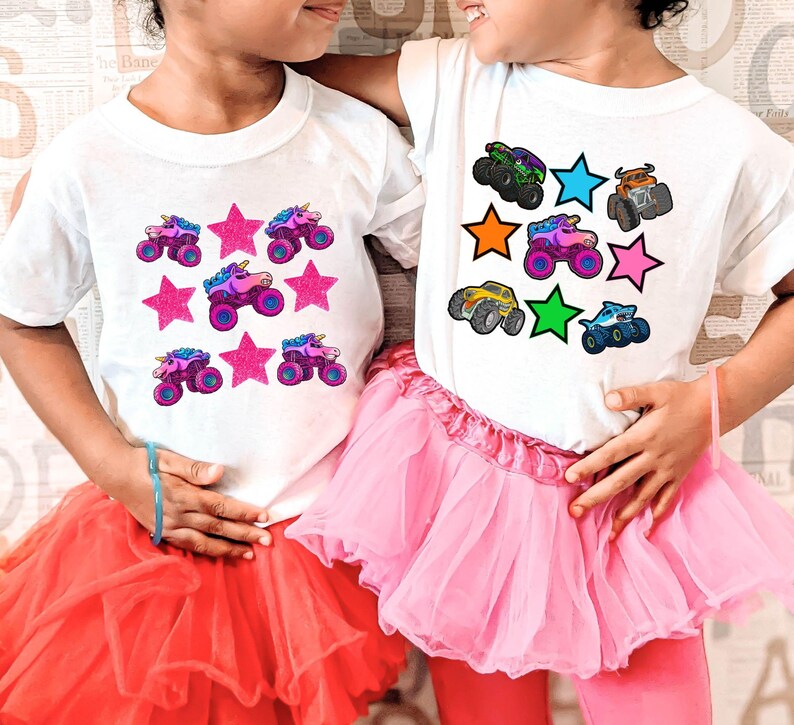 May include: Two children wearing white t-shirts with colorful graphics. One shirt features pink stars and unicorn monster trucks, the other has monster trucks and stars in various colors. Both are paired with pink tutus.
