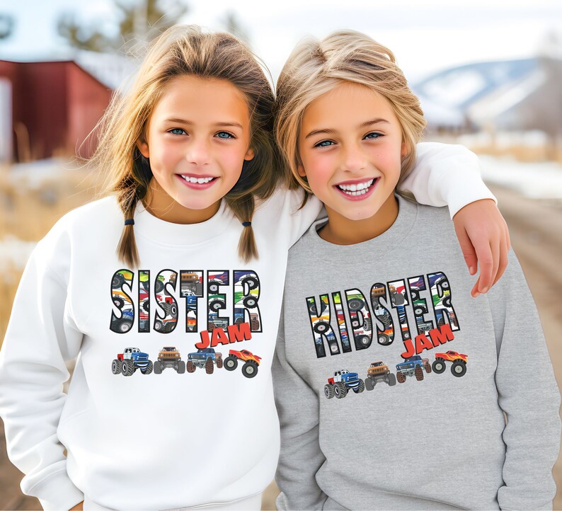 May include: Two children wearing gray and white sweatshirts with a monster truck design. The text on the sweatshirts reads "Kidster Jam" and "Sister Jam".