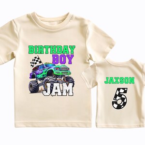 Puede incluir: Dos camisetas de color crema con un gr&aacute;fico de cami&oacute;n monstruo y el texto "Birthday Boy Jam" en la parte delantera y el texto "Jaxson 5" en la parte posterior.