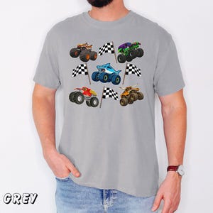 May include: A grey t-shirt featuring colorful monster truck graphics with checkered flags. The trucks are in various colors, including orange, green, and blue, and have unique designs. The word "GREY" is printed at the bottom left.