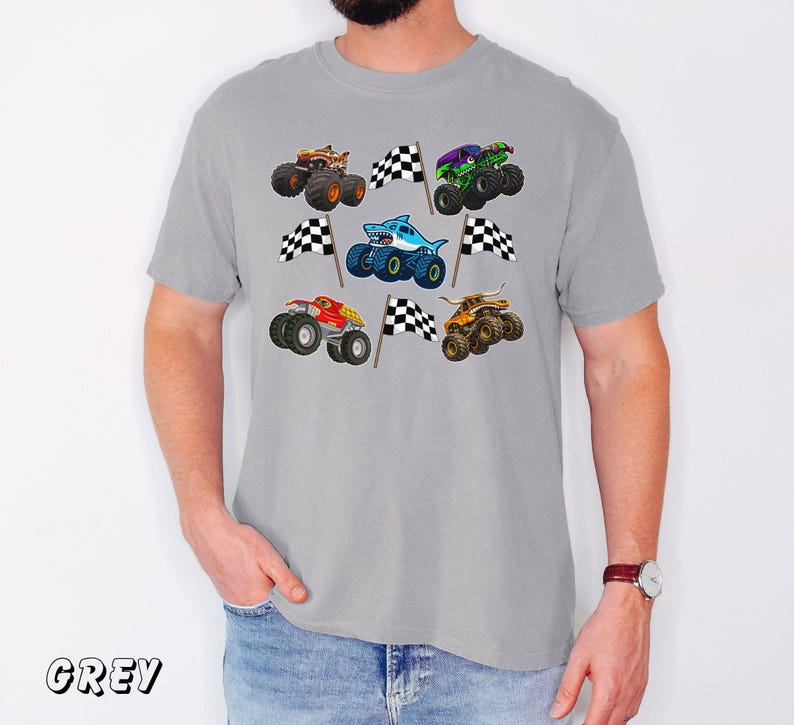 May include: A grey t-shirt featuring colorful monster truck graphics with checkered flags. The trucks are in various colors, including orange, green, and blue, and have unique designs. The word "GREY" is printed at the bottom left.