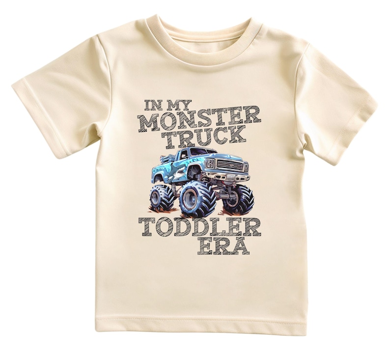 Puede incluir: Una camiseta beige claro para ni&ntilde;os peque&ntilde;os con un gr&aacute;fico de cami&oacute;n monstruo azul y el texto "In My Monster Truck Toddler Era".