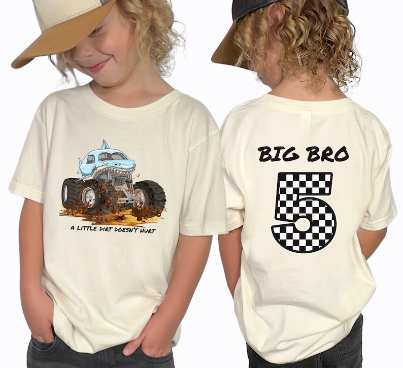 a boy wearing a natural beige colored t-shirt showing front and back print . the front has a megalodon shark monster truck that says a "little dirt doesn't hurt" with a dirt floor and mud and dirt flying around it. The back of the shirt is a personalized name in black that says "Big Bro" and a checkered number 5. Any Name and Age can be applied. Adult , child, toddler and infant sizes.