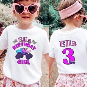 Puede incluir: Camiseta blanca con un gr&aacute;fico colorido que presenta un cami&oacute;n monstruo unicornio y el texto "Ella Birthday Girl". La parte posterior de la camiseta muestra el nombre "Ella" y el n&uacute;mero "3" en rosa.