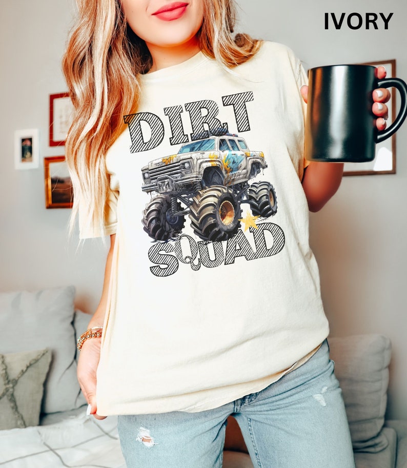 Puede incluir: Camiseta de color marfil con un gr&aacute;fico de monster truck y las palabras "DIRT SQUAD" en negrita y con contorno. El monster truck tiene detalles en azul y amarillo. La camiseta es de corte holgado.