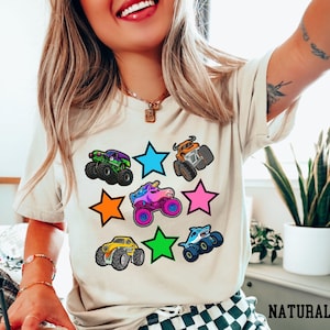 Woman wearing a natural colored t-shirt with 3 rows of fun monster trucks and brightly colored stars