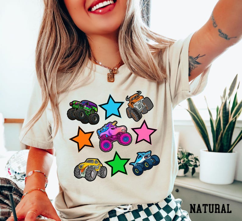 Woman wearing a natural colored t-shirt with 3 rows of fun monster trucks and brightly colored stars