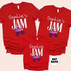 May include: Red t-shirts with the text "Sophia's JAM" in white, featuring a cartoon unicorn monster truck. The shirts are short-sleeved and suitable for a family or group. The design includes a colorful unicorn and truck.