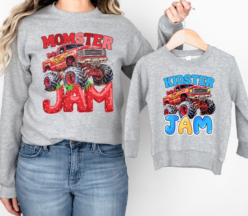 May include: Two gray sweatshirts with matching designs. One sweatshirt features the text "MOMSTER JAM" with a red monster truck graphic. The other sweatshirt has the text "KIDSTER JAM" with a similar truck graphic. Both sweatshirts are long-sleeved.