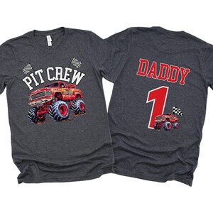 以下が含まれることがあります： モンスタートラックをテーマにしたグレーのTシャツ2枚。1枚は「ピットクルー」と赤いモンスタートラックと市松模様の旗が書かれている。もう1枚は「ダディ」と数字の「1」と、より小さい赤いモンスタートラックが書かれている。