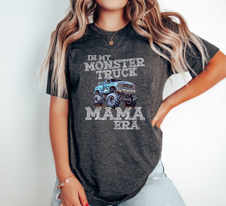 Puede incluir: Una camiseta gris oscuro con un gr&aacute;fico de cami&oacute;n monstruo azul y el texto "In My Monster Truck Mama Era".