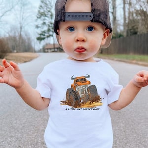 Cute boy wearing a white tee with an orange bull monster truck with the text "A little dirt doesn't hurt" underneath the graphic