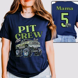 Op de afbeelding: Marineblauw T-shirt met een groen en wit "PIT CREW"-motief en een monster truck illustratie. De achterkant van het shirt heeft het woord "Mama", het nummer "5" en een monster truck afbeelding.
