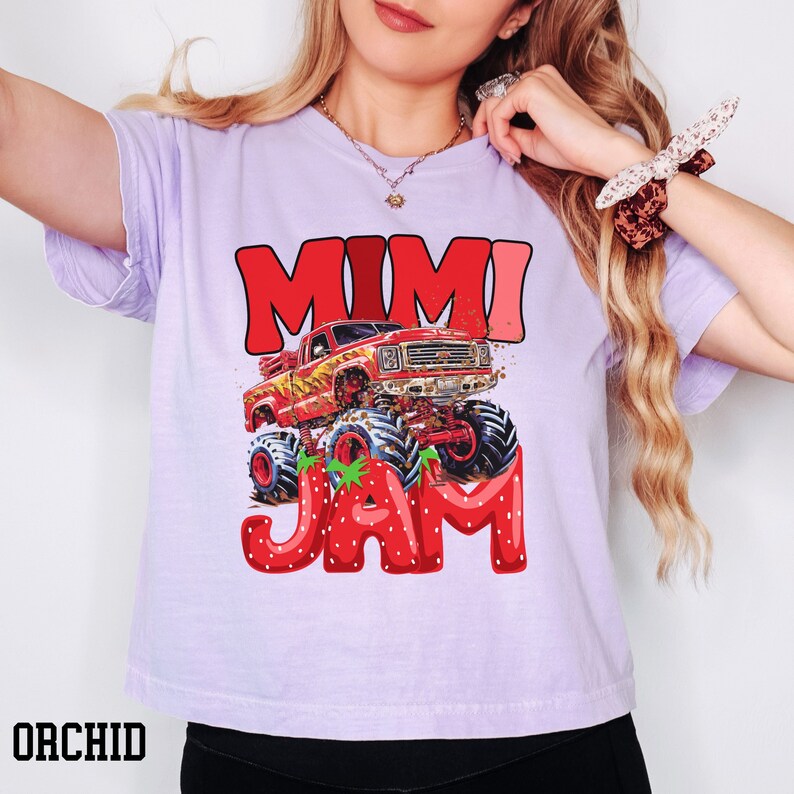 May include: A purple t-shirt with a red monster truck graphic and the text "Mimi Jam" in red and white letters. The monster truck is driving through a strawberry field.