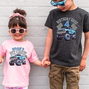 May include: Two children wearing graphic t-shirts. The pink shirt says "Noah's Pit Crew" with a blue monster truck graphic. The gray shirt says "Birthday Dude 4" with a blue monster truck graphic. Both shirts have checkered flags.