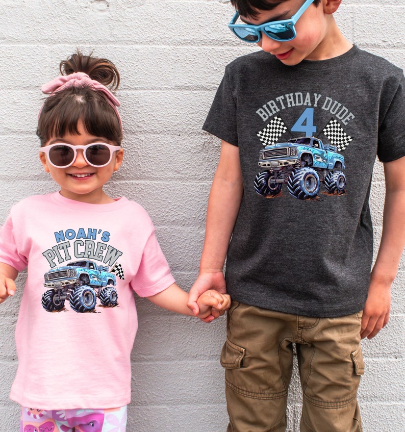 May include: Two children wearing graphic t-shirts. The pink shirt says "Noah's Pit Crew" with a blue monster truck graphic. The gray shirt says "Birthday Dude 4" with a blue monster truck graphic. Both shirts have checkered flags.