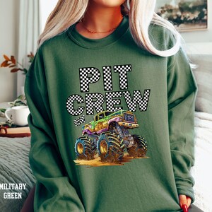 May include: Green sweatshirt with a black and white checkered "PIT CREW" graphic and a cartoon monster truck.