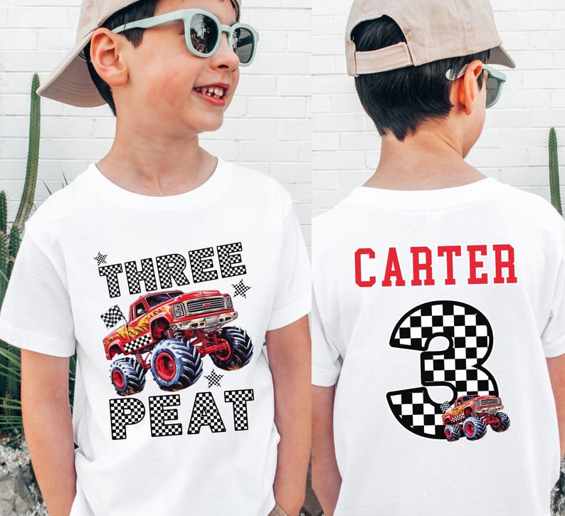 Pictured is a boy wearing a light colored t-shirt which says THREE PEAT in black ans white checkered letters along with a big red monster truck graphic and black and white checkered stars and flag. On the back of the shirt is custom name CARTER in red and a black and white checkered number 3