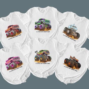 Peut inclure: T-shirts blancs avec des motifs de monster trucks color&eacute;s. Chaque t-shirt pr&eacute;sente un design de camion diff&eacute;rent avec de grandes roues et le texte "A LITTLE DIRT DOESN'T HURT". Les camions sont rouges, roses, verts et bleus.