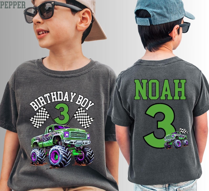 Pode incluir: Camiseta cinza escuro com um gr&aacute;fico de monster truck verde e roxo. A frente da camisa diz "BIRTHDAY BOY 3" com bandeiras quadriculadas. A parte de tr&aacute;s da camisa diz "NOAH 3".