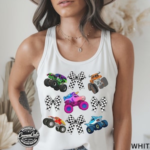 May include: White vest top with colourful monster truck designs and chequered bows. The trucks are in green, orange, red, blue, and purple. The text "DESIGNED BY COMMON CODE" is visible.