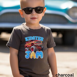 May include: A charcoal grey t-shirt with a red monster truck graphic and the text "Kidster Jam" in blue and yellow letters.