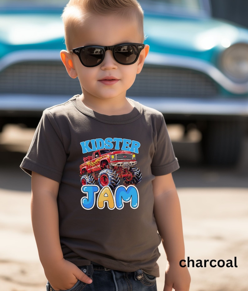 May include: A charcoal grey t-shirt with a red monster truck graphic and the text "Kidster Jam" in blue and yellow letters.