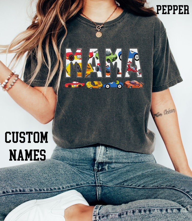May include: A gray t-shirt with the word "MAMA" spelled out in white letters.  Each letter is made up of a different cartoon race car.  The text "CUSTOM NAMES" is printed below the shirt.