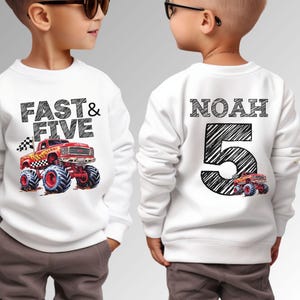 Op de afbeelding: Witte sweatshirt met een afbeelding van een rode monstertruck met blauwe banden. De voorkant toont "FAST & FIVE" in zwarte tekst. De achterkant van het shirt zegt "NOAH 5" met een kleinere monstertruck-afbeelding.