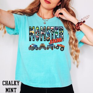 K&ouml;nnte beinhalten: Ein t&uuml;rkisfarbenes T-Shirt mit dem Aufdruck "Monster Jam" auf der Vorderseite. Die W&ouml;rter bestehen aus Bildern von Monstertrucks.