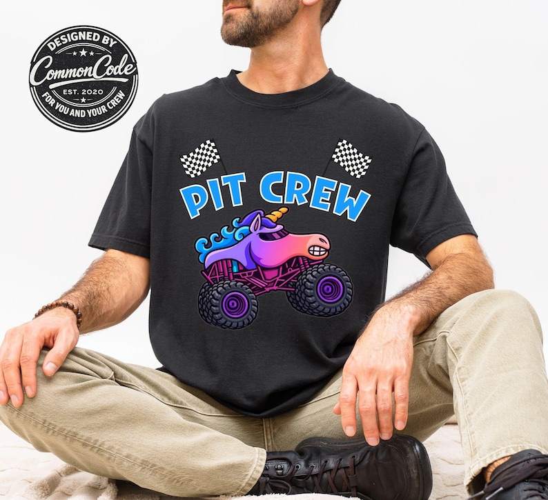 May include: Black t-shirt with the words "PIT CREW" in blue and white, featuring a cartoon unicorn monster truck. The unicorn is purple, pink, and blue, with a yellow horn. Checkered flags are on the top of the shirt.