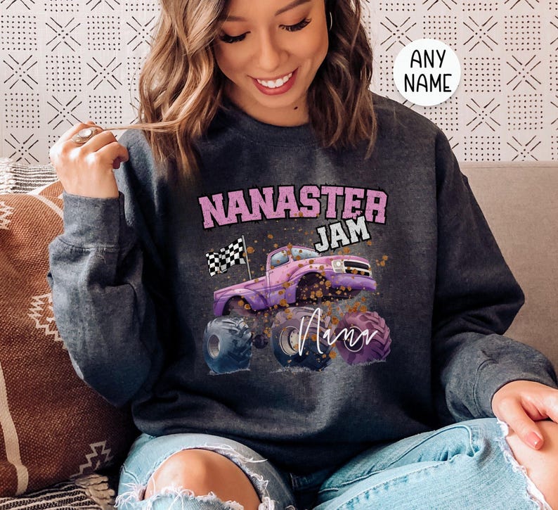 Pu&ograve; includere: Una felpa grigia scura con una grafica rosa e bianca di un monster truck con il testo "Nana's Jam" e la parola "Ann" scritta in corsivo.