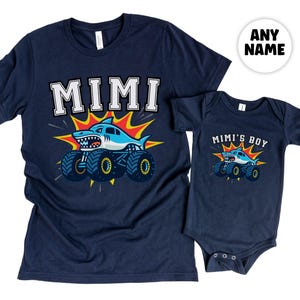 Pictured is a t-shirt adult size in Navy that says "MIMI" and a baby bodysuit in navy that says "Mimi's Boy" - both have a shark monster truck underneath with an explosion of orange and yellow behind the truck. Any Custom Name. Family Sizes available.